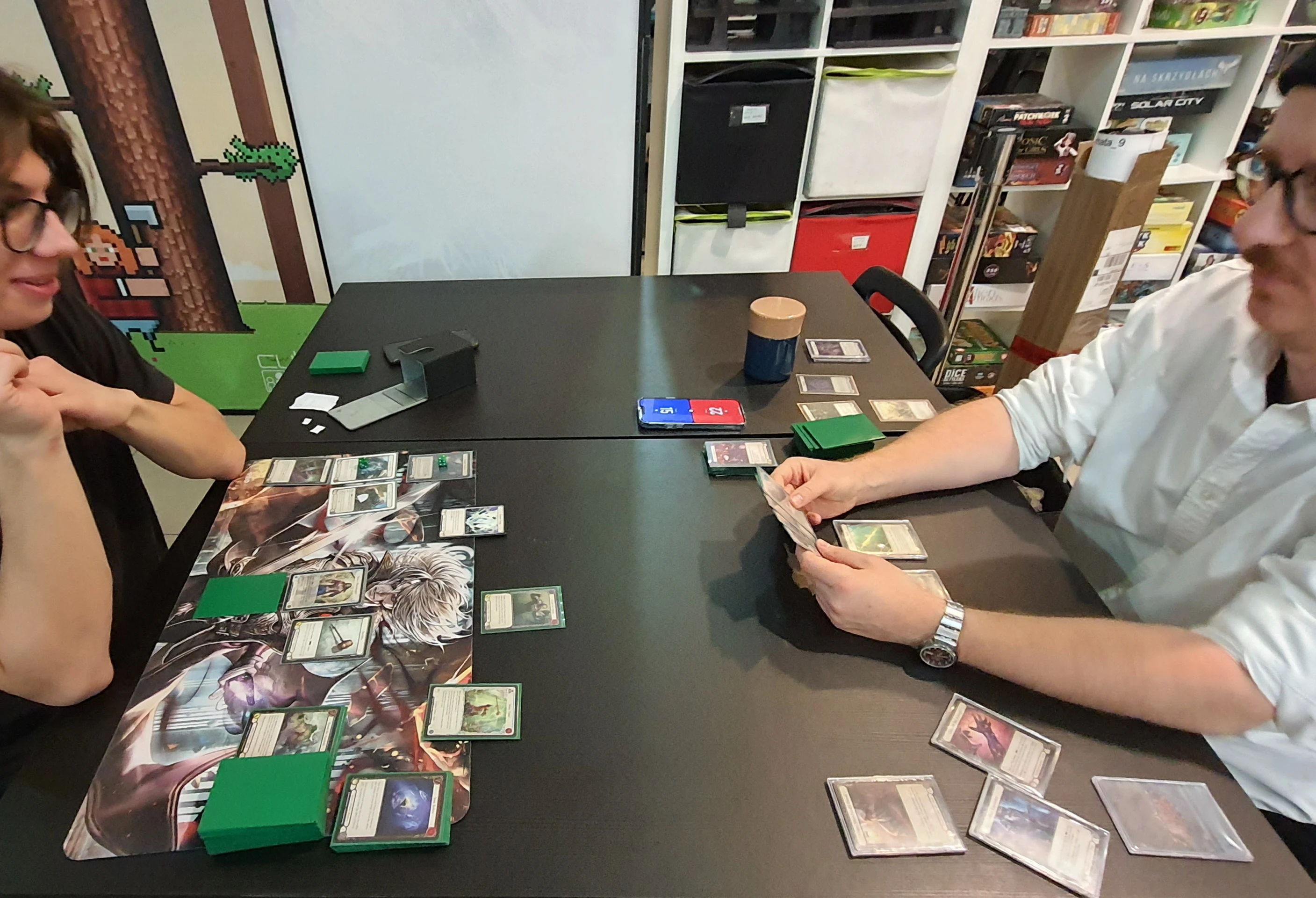紙TCGの対戦中に、物理カードとスリーブ付きデッキを卓上で扱う様子